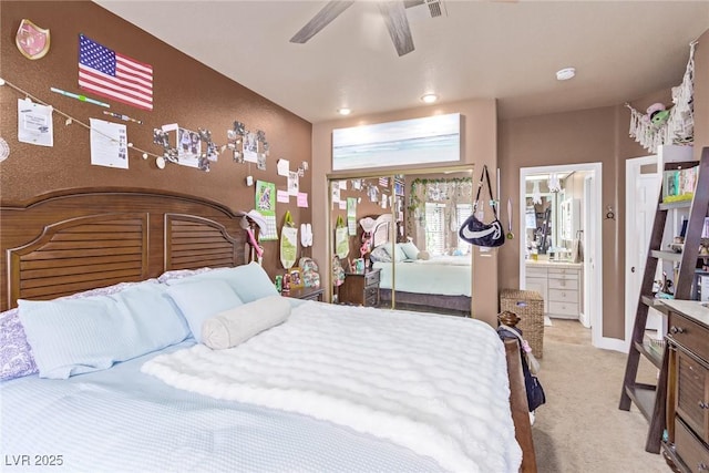 bedroom with ceiling fan, light colored carpet, and ensuite bath