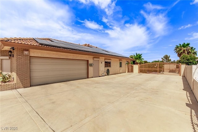 view of front of property featuring driveway, roof mounted solar panels, a gate, and brick siding