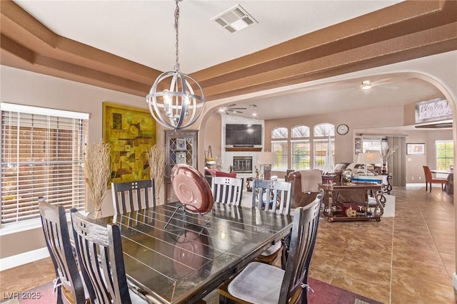 tiled dining area with a glass covered fireplace, visible vents, baseboards, and ceiling fan with notable chandelier