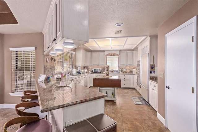 kitchen with stainless steel dishwasher, sink, light tile patterned floors, white cabinets, and a center island