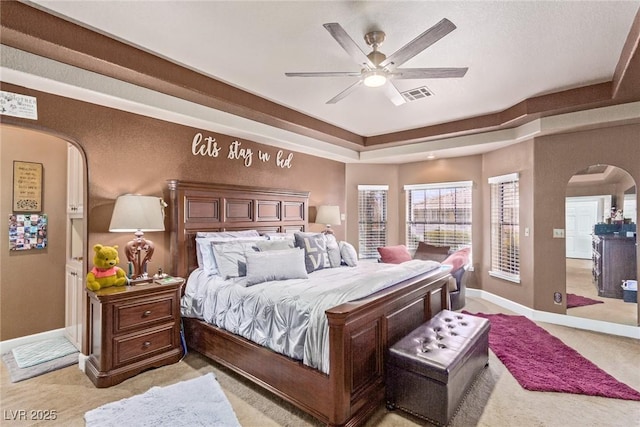 bedroom featuring a raised ceiling, ceiling fan, and light carpet