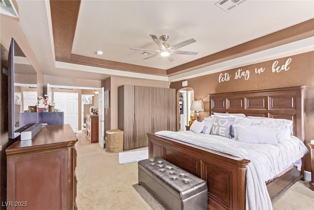 bedroom with a tray ceiling, ceiling fan, and light carpet