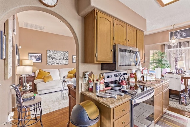 kitchen featuring light stone countertops, appliances with stainless steel finishes, pendant lighting, a chandelier, and light hardwood / wood-style floors