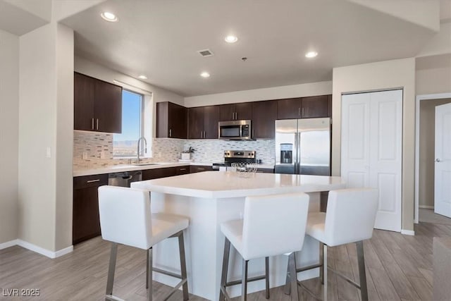 kitchen with appliances with stainless steel finishes, a kitchen island, light hardwood / wood-style floors, sink, and a breakfast bar