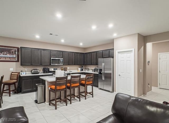 kitchen with appliances with stainless steel finishes, a kitchen breakfast bar, an island with sink, and dark brown cabinets