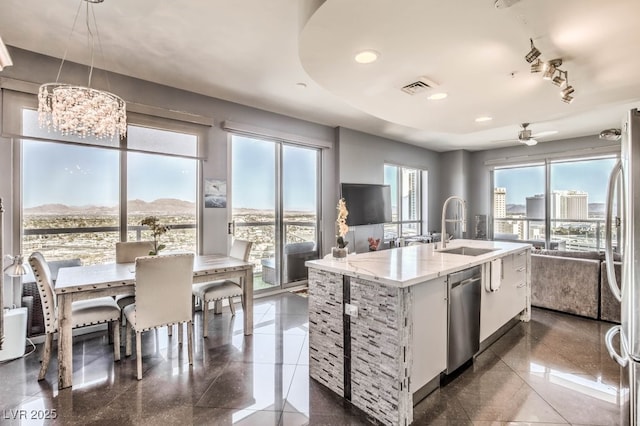 kitchen featuring ceiling fan with notable chandelier, pendant lighting, stainless steel appliances, sink, and a center island with sink