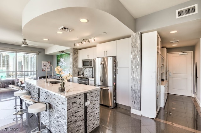 kitchen featuring an island with sink, appliances with stainless steel finishes, tasteful backsplash, white cabinets, and a breakfast bar