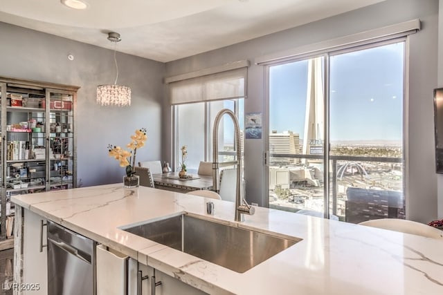 kitchen featuring decorative light fixtures, light stone counters, sink, and stainless steel dishwasher