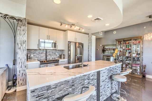 kitchen with a kitchen bar, sink, appliances with stainless steel finishes, white cabinets, and light stone counters