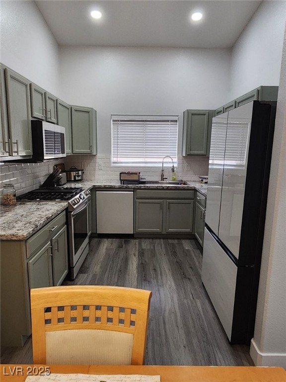 kitchen featuring sink, light stone counters, appliances with stainless steel finishes, tasteful backsplash, and dark hardwood / wood-style flooring