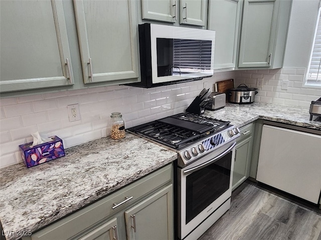 kitchen with light stone countertops, decorative backsplash, dark hardwood / wood-style flooring, and stainless steel stove