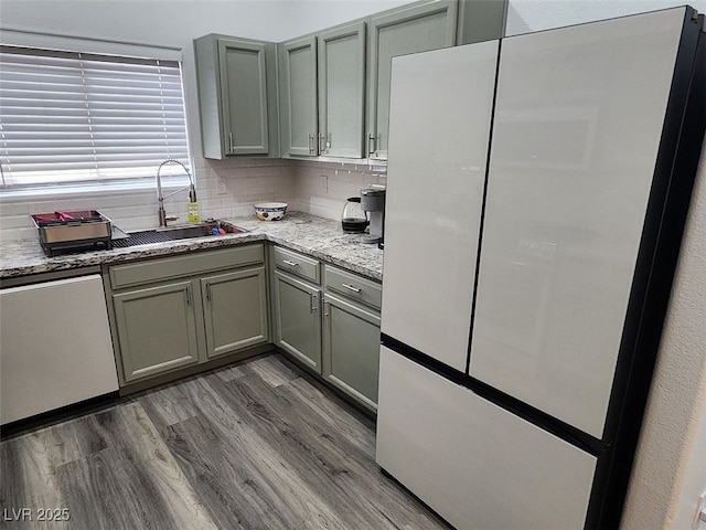 kitchen featuring dishwasher, sink, tasteful backsplash, white fridge, and light stone counters