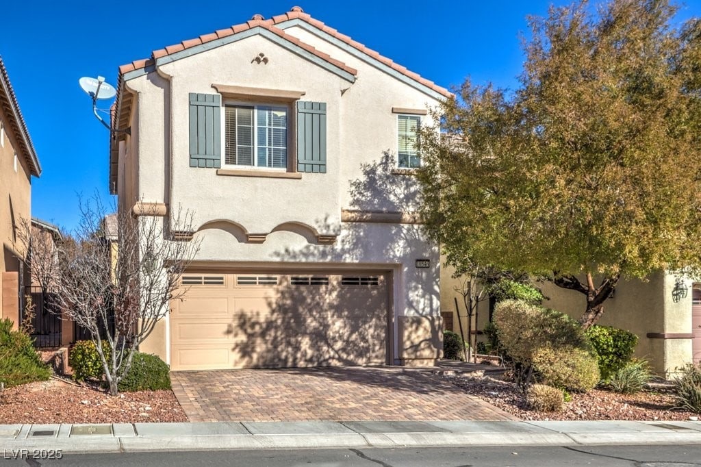 mediterranean / spanish-style house with an attached garage, a tiled roof, decorative driveway, and stucco siding