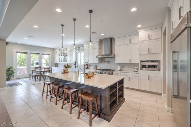 kitchen with a spacious island, wall chimney range hood, light tile patterned floors, white cabinetry, and stainless steel appliances