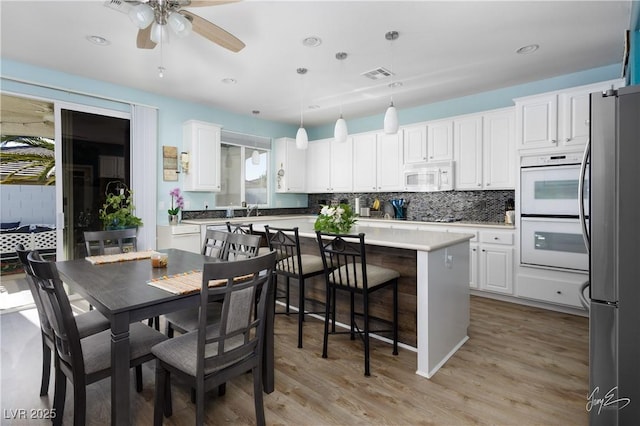 kitchen featuring white appliances, a center island, white cabinetry, decorative light fixtures, and light hardwood / wood-style floors