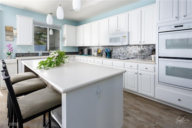 kitchen with white appliances, white cabinetry, pendant lighting, and a center island