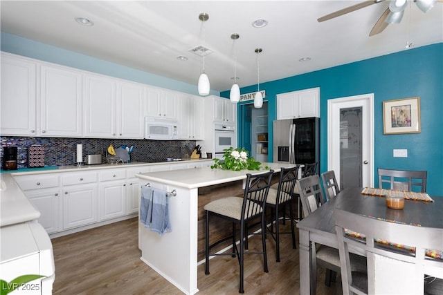 kitchen featuring a kitchen island, white appliances, pendant lighting, and white cabinetry