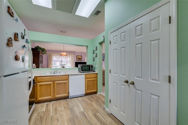 kitchen with decorative light fixtures, white appliances, sink, and light hardwood / wood-style flooring