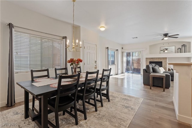 dining space featuring ceiling fan with notable chandelier, light wood-type flooring, and a fireplace