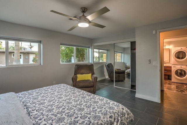 bedroom with ceiling fan, stacked washer / dryer, a closet, and dark tile patterned flooring