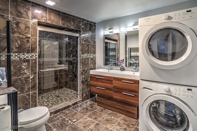 bathroom featuring toilet, stacked washer / drying machine, a shower with door, a textured ceiling, and vanity