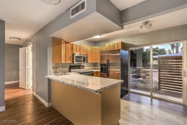 kitchen with appliances with stainless steel finishes, light brown cabinets, sink, kitchen peninsula, and light stone counters