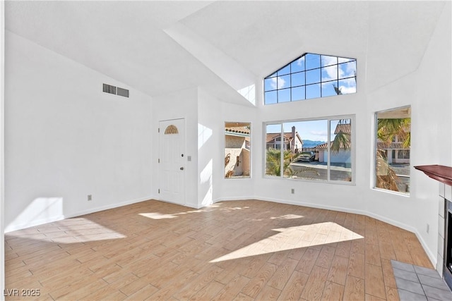 unfurnished living room with a tiled fireplace, a towering ceiling, and light hardwood / wood-style floors