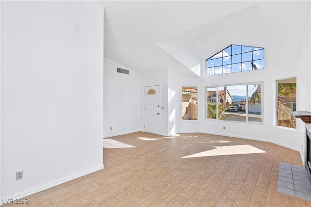 unfurnished living room with high vaulted ceiling, a tile fireplace, and light wood-type flooring