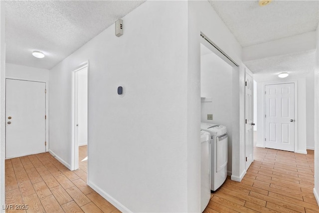 hallway featuring washing machine and dryer, a textured ceiling, and light hardwood / wood-style floors