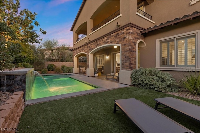 pool at dusk with pool water feature and a patio area