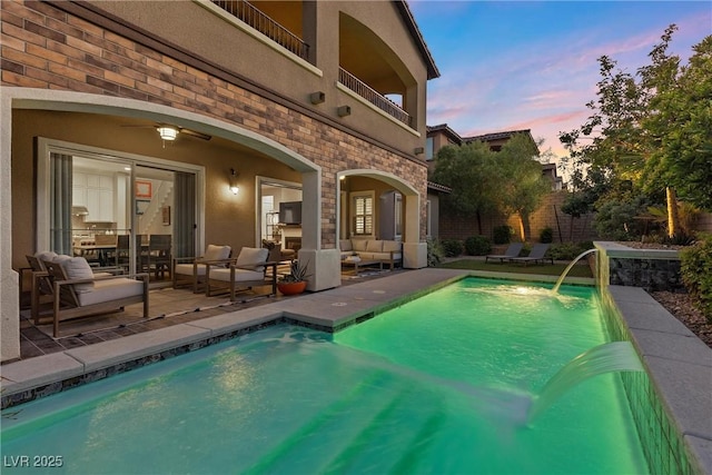 pool at dusk featuring a patio, an outdoor hangout area, and pool water feature