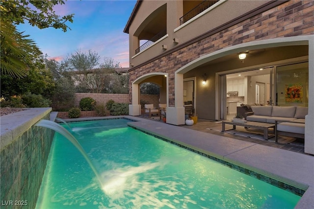 pool at dusk featuring pool water feature, outdoor lounge area, and a patio