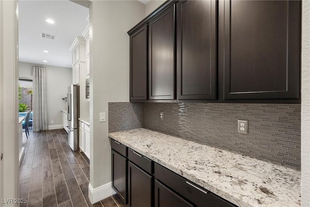 kitchen featuring decorative backsplash, stainless steel fridge with ice dispenser, dark brown cabinetry, and light stone counters