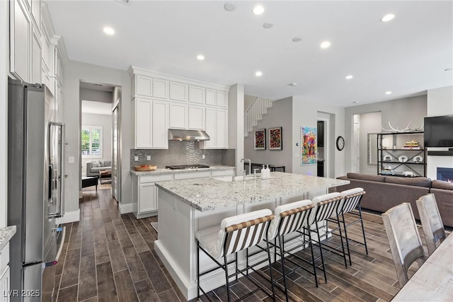 kitchen with light stone counters, an island with sink, appliances with stainless steel finishes, a kitchen bar, and white cabinetry