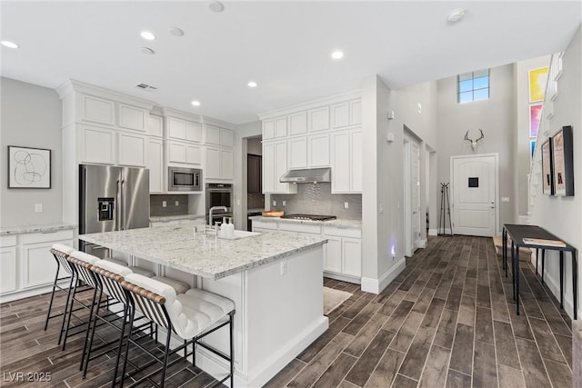 kitchen featuring light stone countertops, a kitchen breakfast bar, a center island with sink, white cabinets, and appliances with stainless steel finishes