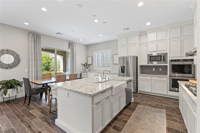 kitchen featuring sink, light stone counters, an island with sink, white cabinets, and appliances with stainless steel finishes