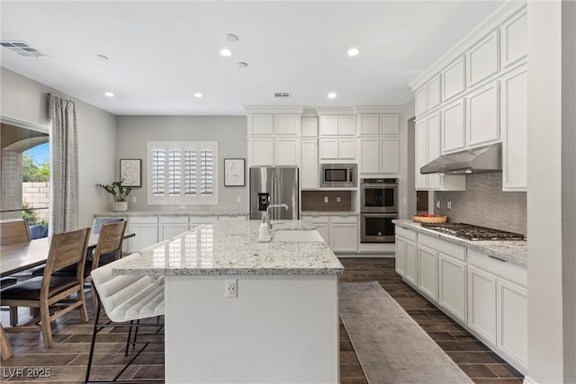 kitchen with white cabinets, light stone counters, stainless steel appliances, and a kitchen island with sink