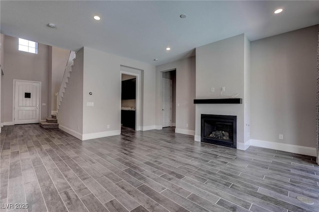 unfurnished living room with baseboards, a fireplace, and stairs