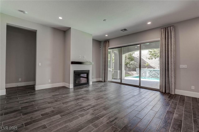 unfurnished living room featuring recessed lighting, visible vents, baseboards, a glass covered fireplace, and dark wood-style flooring