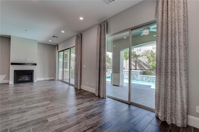 unfurnished living room with baseboards, a glass covered fireplace, wood finished floors, and visible vents