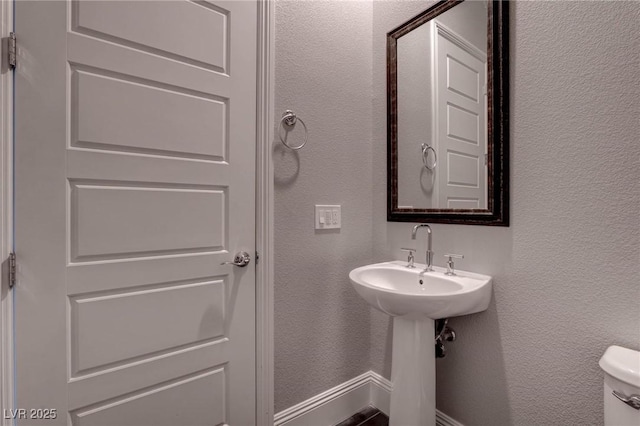 half bathroom with a textured wall, baseboards, and toilet