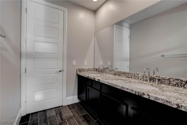 bathroom featuring wood tiled floor, baseboards, a sink, and double vanity