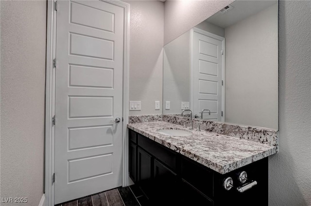 bathroom featuring visible vents, a textured wall, wood finished floors, and vanity