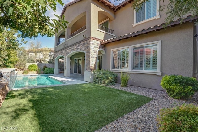 rear view of property featuring a balcony, a tiled roof, a yard, a fenced in pool, and stucco siding