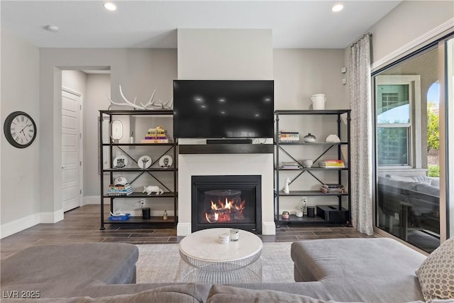living area with baseboards, a glass covered fireplace, wood finished floors, and recessed lighting