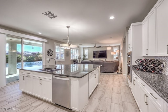 kitchen featuring dark stone counters, sink, a center island with sink, dishwasher, and white cabinetry