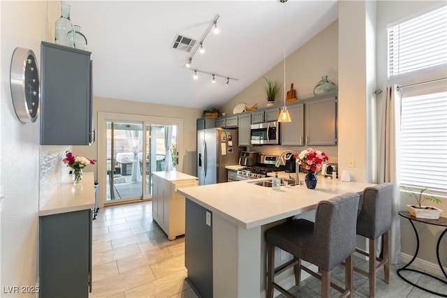 kitchen with kitchen peninsula, appliances with stainless steel finishes, a kitchen bar, gray cabinetry, and decorative light fixtures