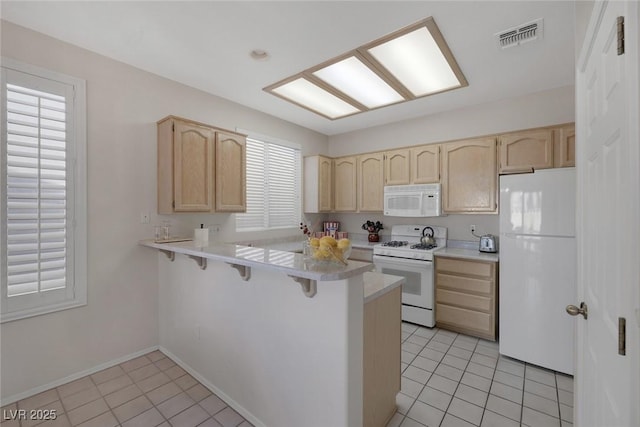 kitchen featuring a breakfast bar, light tile patterned flooring, white appliances, and kitchen peninsula