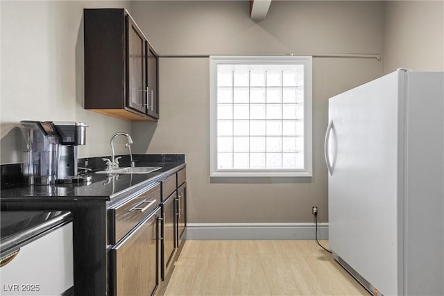 kitchen with light wood-type flooring, dark brown cabinets, white refrigerator, and sink