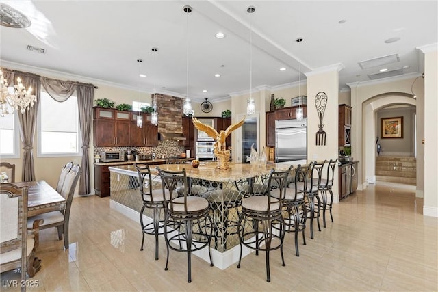 kitchen with light stone countertops, ornamental molding, stainless steel appliances, a spacious island, and pendant lighting